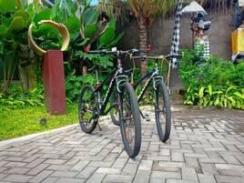 Una bicicleta estacionada en un área pavimentada con follaje y una estructura decorativa al fondo.