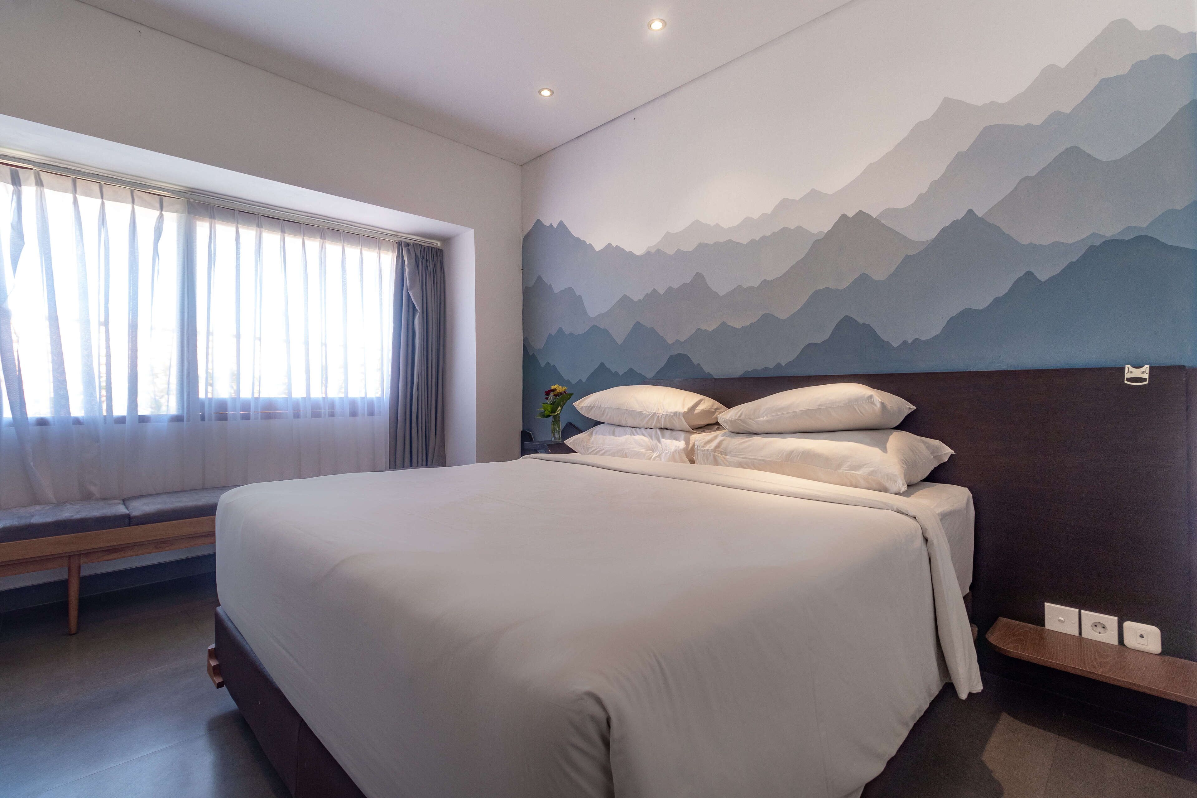 A modern bedroom with a large bed, a bench by the window, and a mountain mural on the wall.