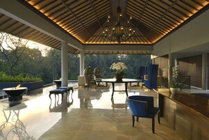 An indoor area with a reflective floor, a table with chairs, a chandelier, and a view of greenery outside.