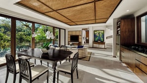 A modern kitchen with a large island, a dining area with a table and chairs, and a living area with a TV and artwork. - Samsara Ubud (Payangan)