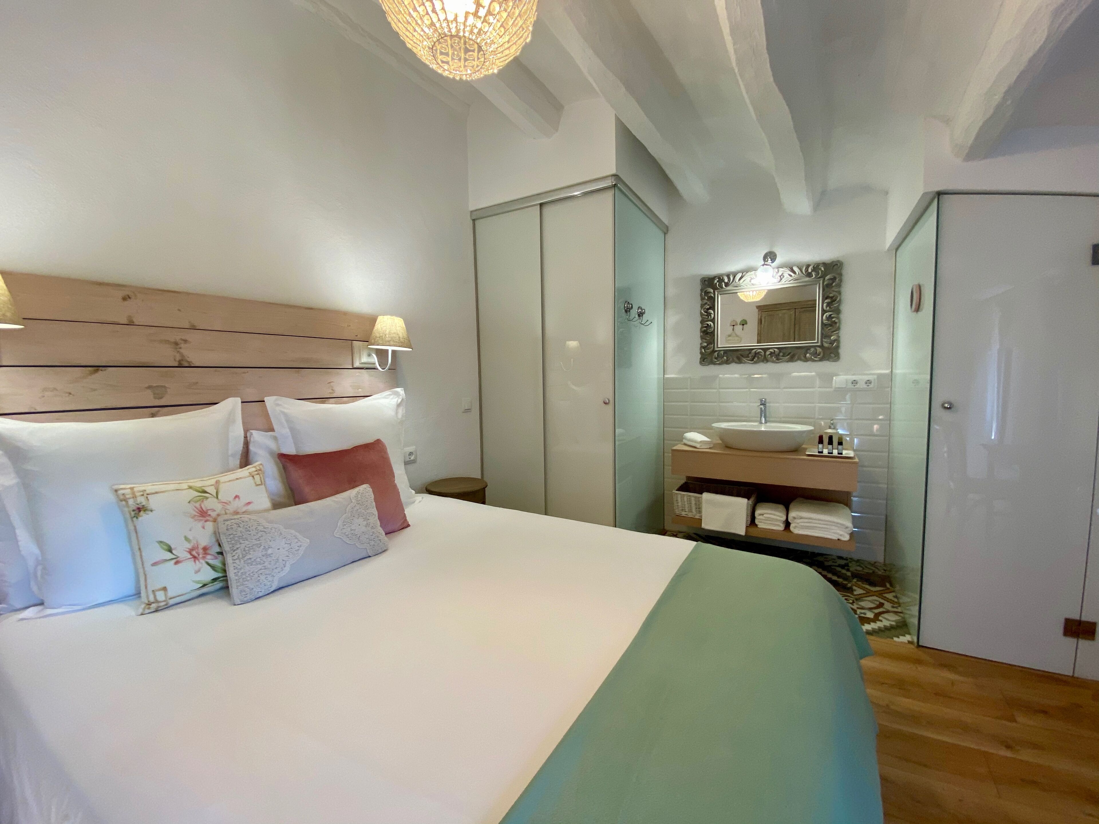 A hotel room with a bed, a bedside lamp, a bathroom with a sink and mirror, and a wardrobe.