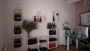 Quarto com prateleiras para vinho, uma escrivaninha com computador e um vaso com flores.