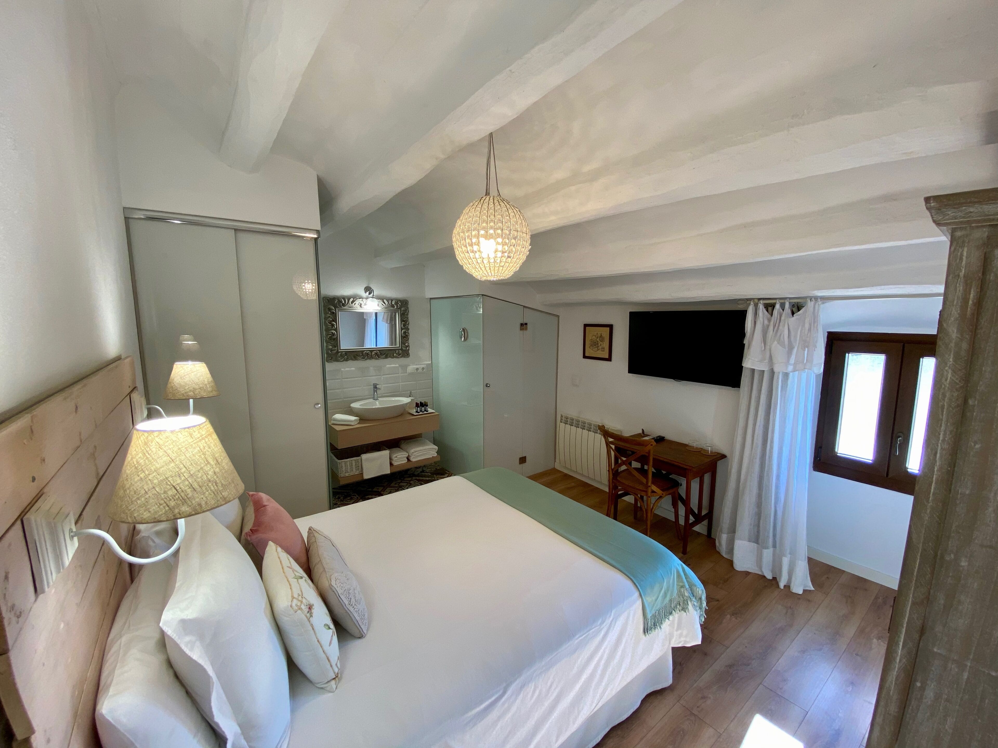 Un dormitorio con cama, lámpara de noche, cómoda, tocador y televisor.