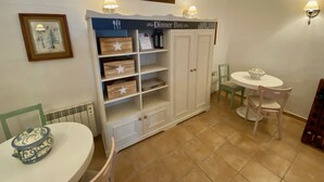 Uma sala de jantar com uma mesa branca, cadeiras, um armário com detalhes em estrela e um quadro na parede.