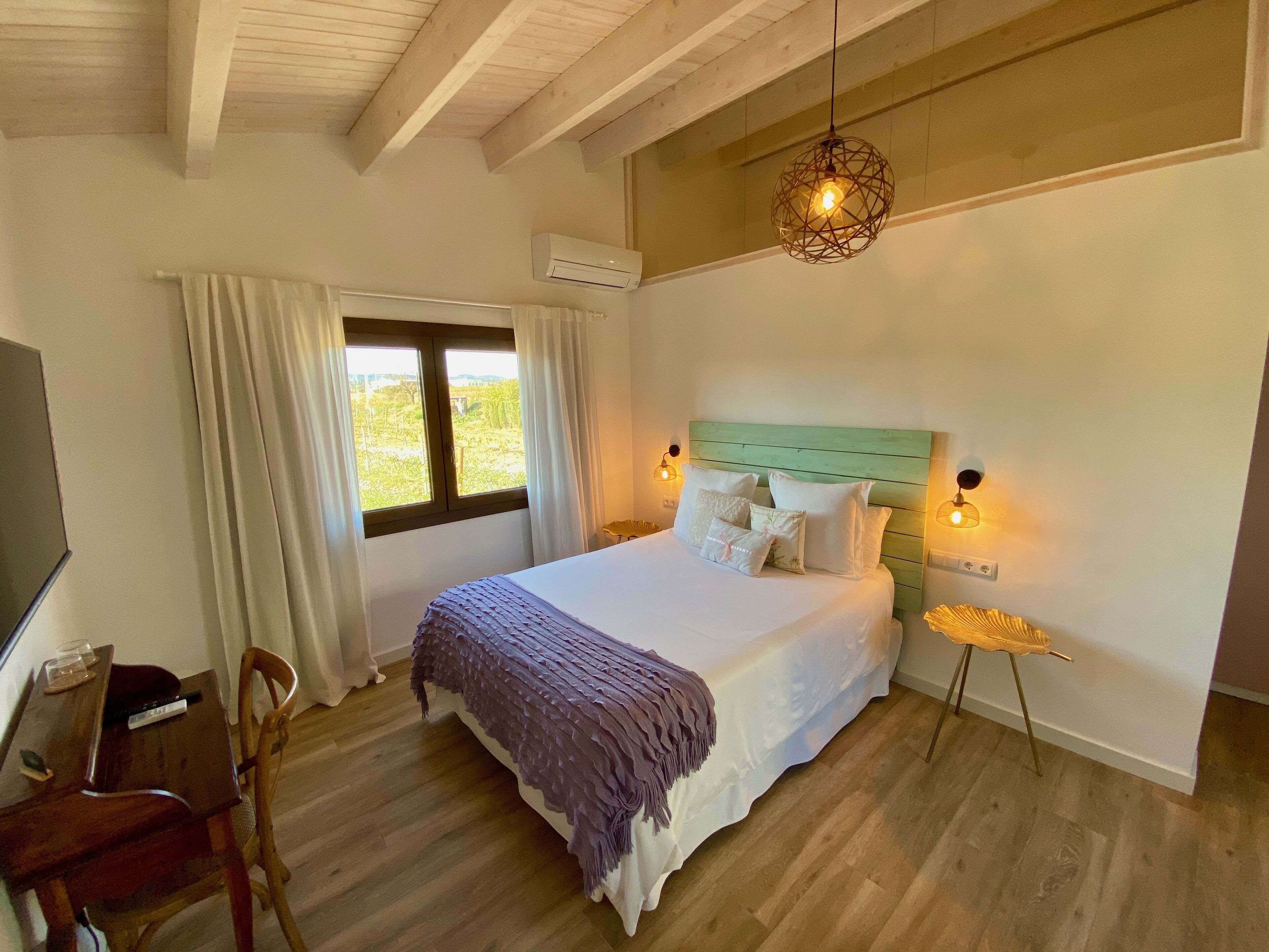 A bedroom with a bed, a desk, a chair, a window with curtains, and a hanging light fixture.