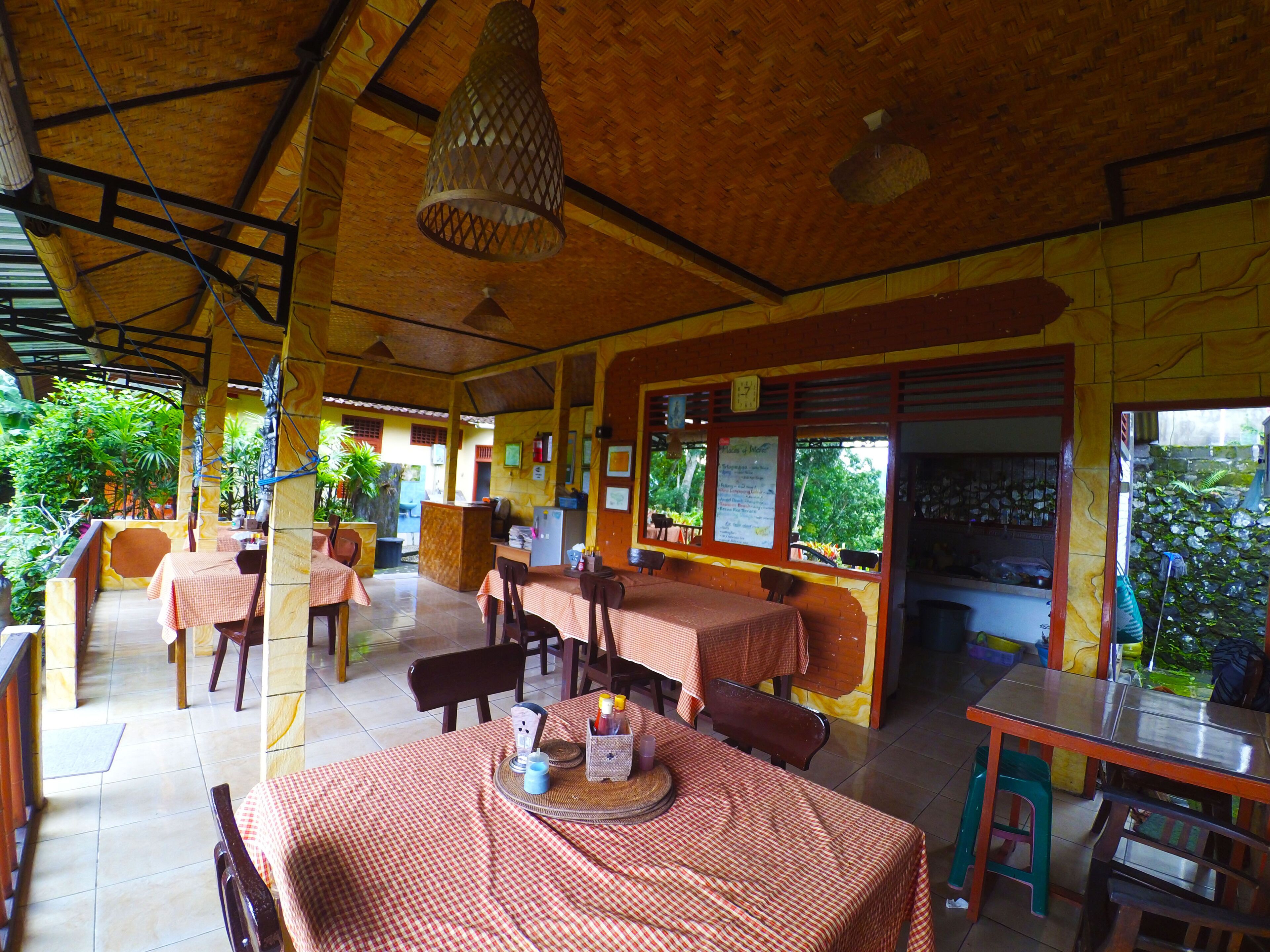 A restaurant with multiple tables and chairs, a wooden ceiling, and a view of greenery outside.