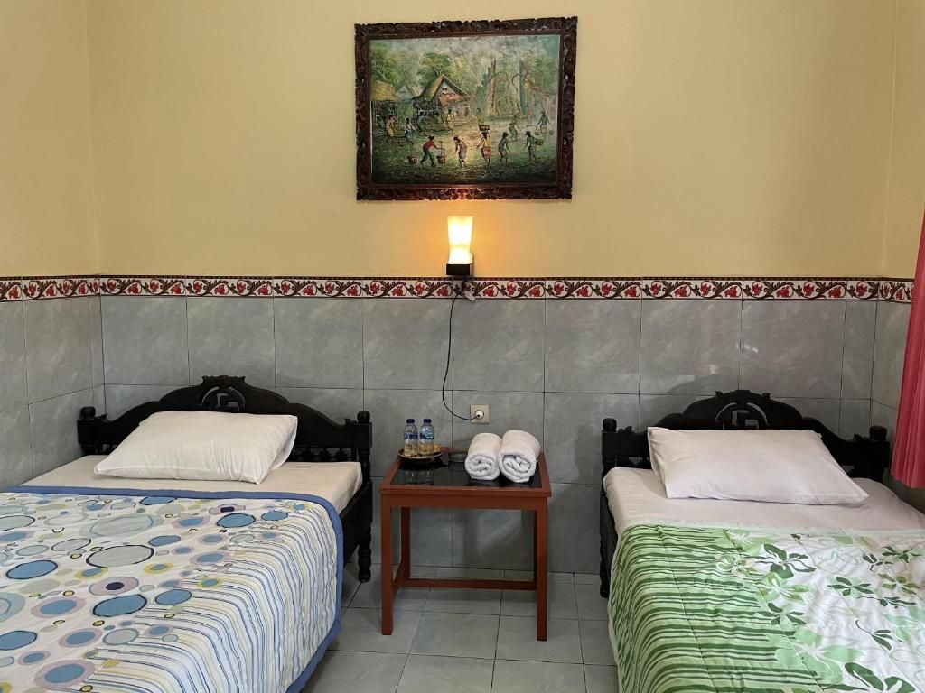 A hotel room with two beds, a nightstand with toiletries, a painting on the wall, and a patterned border along the ceiling.
