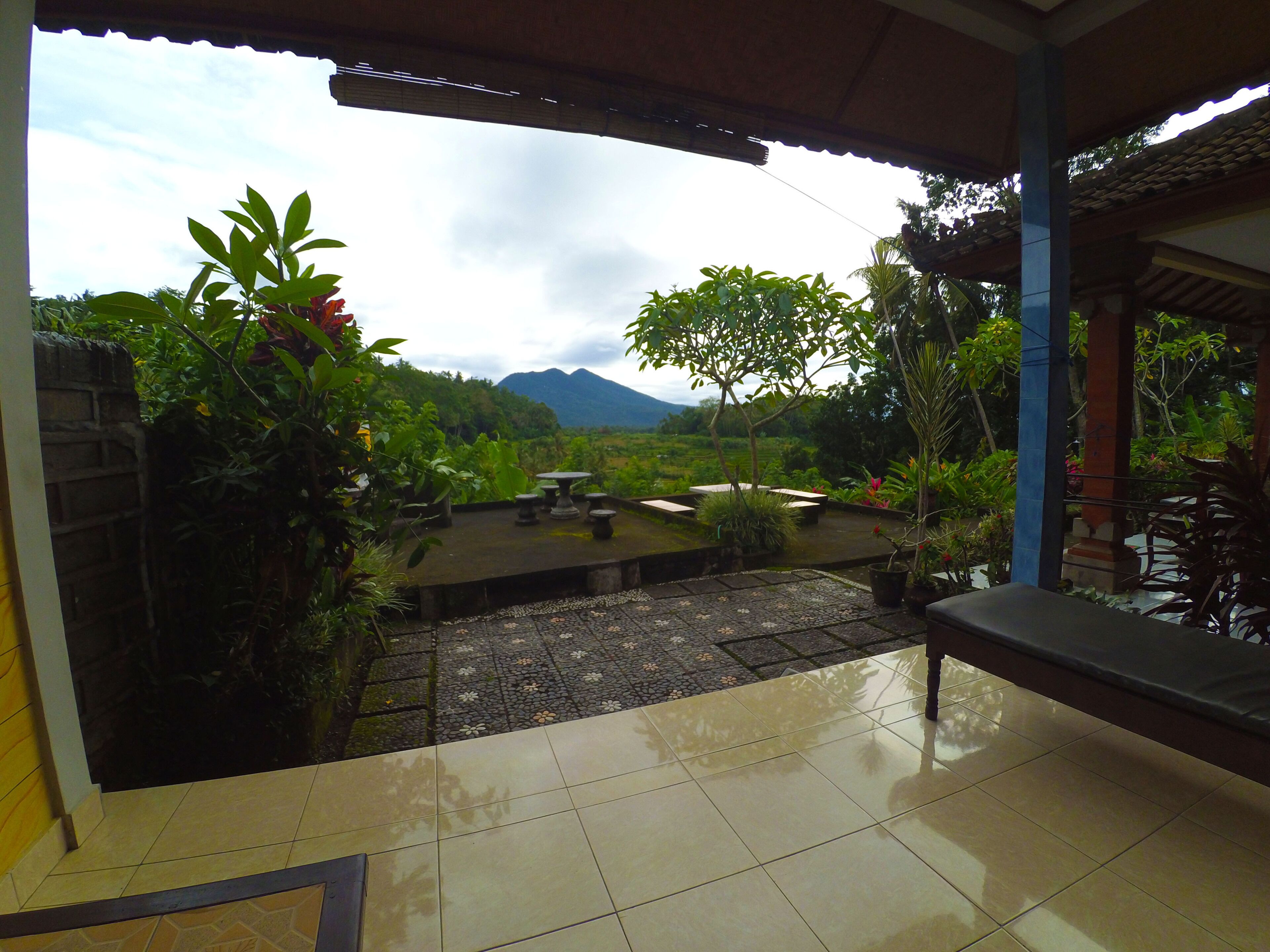 A covered patio with a view of a mountainous landscape, outdoor seating, and potted plants.