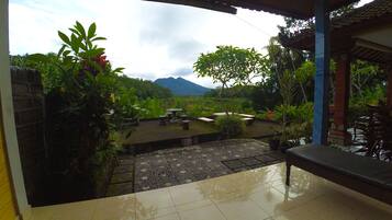 A covered patio with a view of a mountainous landscape, outdoor seating, and potted plants.
