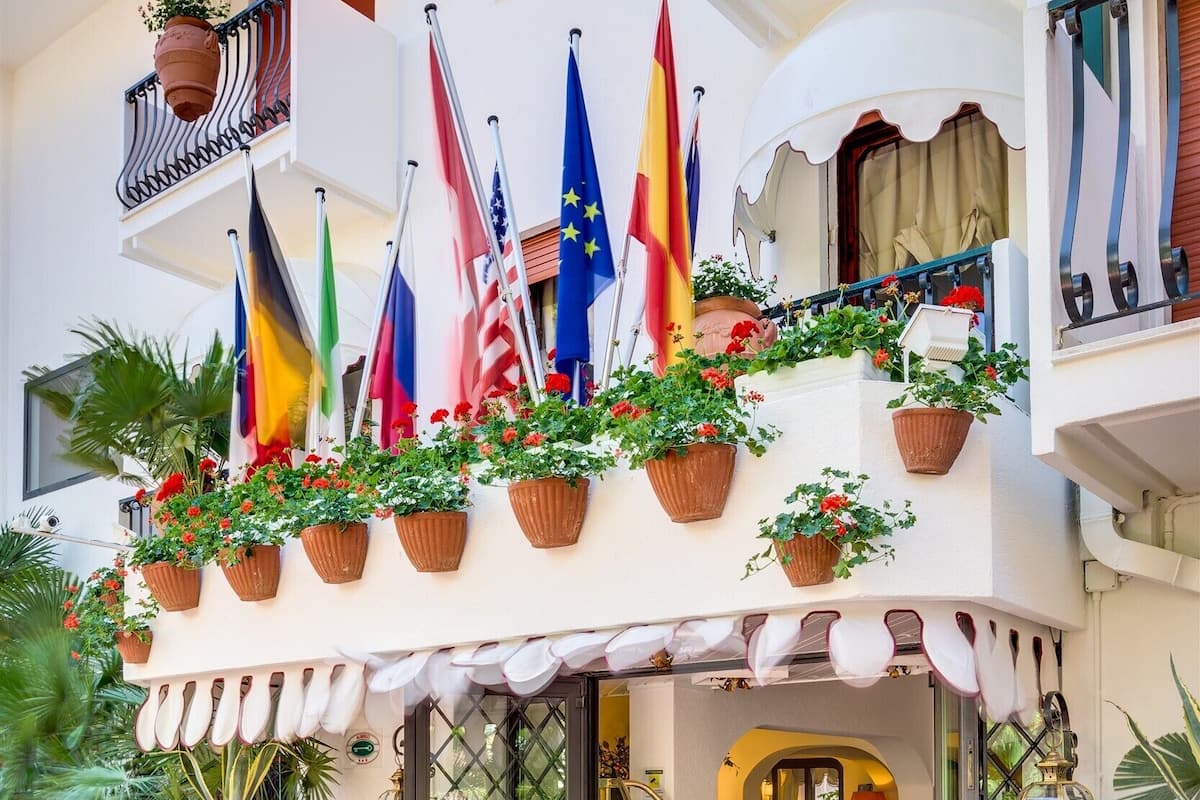 A hotel entrance with multiple flags, potted plants, and a red doormat.