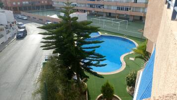 Un edificio residencial con piscina, cancha de baloncesto y calle con automóviles estacionados.