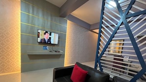 A modern living room with a black leather sofa, a mounted TV, and a blue spiral staircase.