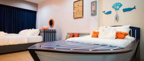 Een hotelkamer met twee bedden, een groot bed met een wit en oranje kussenopstelling en een kleiner bed met witte beddengoed.