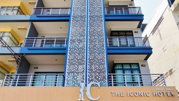 A hotel with a prominent vertical sign featuring a unique pattern, multiple balconies, and a clear entrance with a sign reading "THE ICONIC HOTEL".