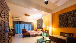 A modern hotel room with a large bed, a sitting area with a sofa and armchair, a small table, and a decorative wall piece.