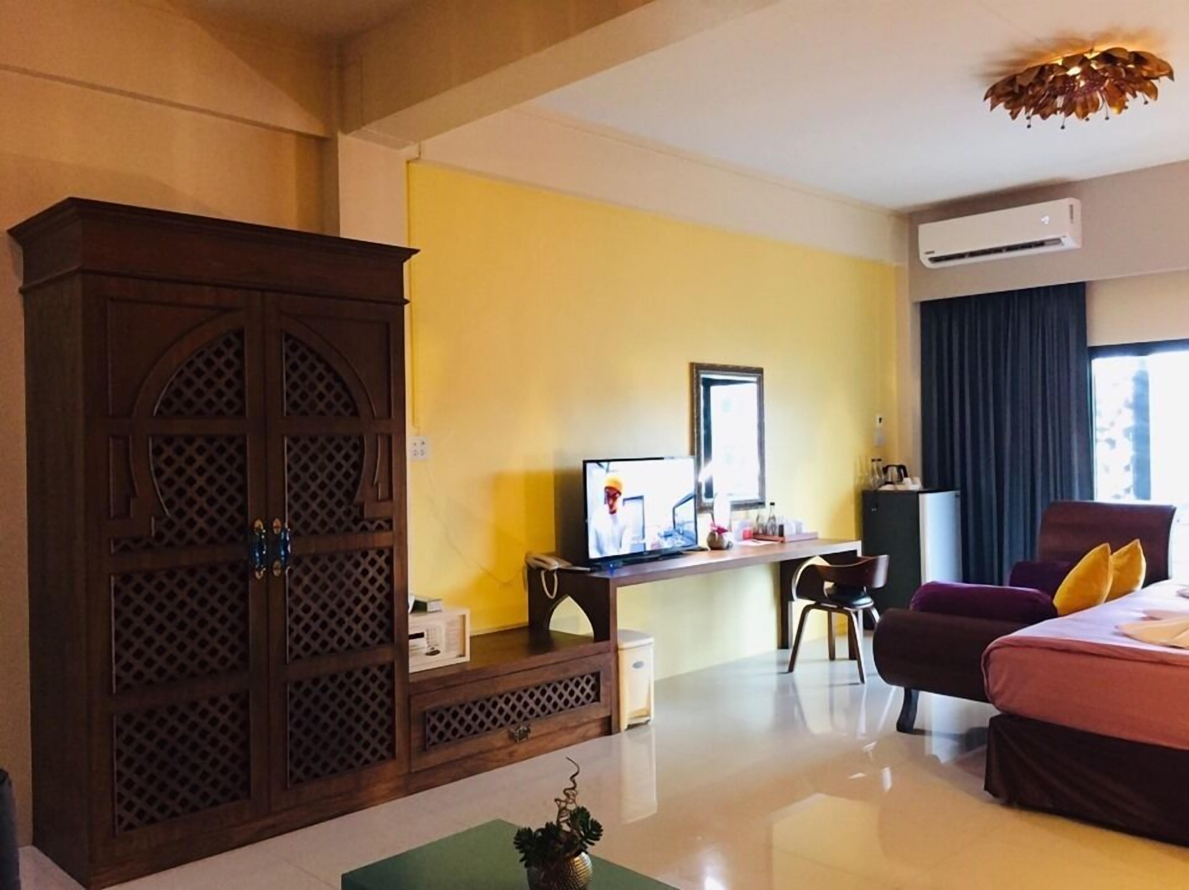 Una habitación de hotel con un armario de madera, un escritorio con computadora, una cama y una silla.