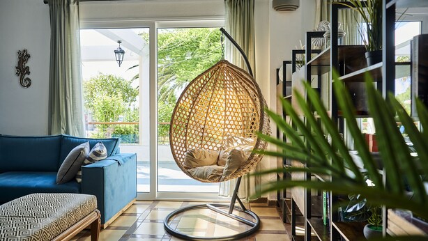 Un salon avec un canapé bleu, un fauteuil suspendu, un pouf à motifs et une bibliothèque.