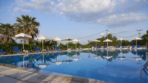 Une piscine bordée de chaises longues bleues et de parasols blancs, entourée de palmiers et de verdure.