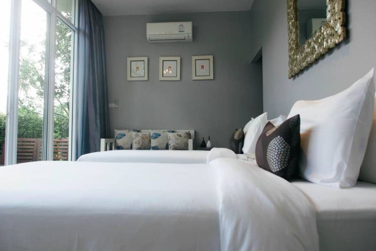 A bedroom with a large bed, a window with curtains, an air conditioning unit, and three framed pictures on the wall.