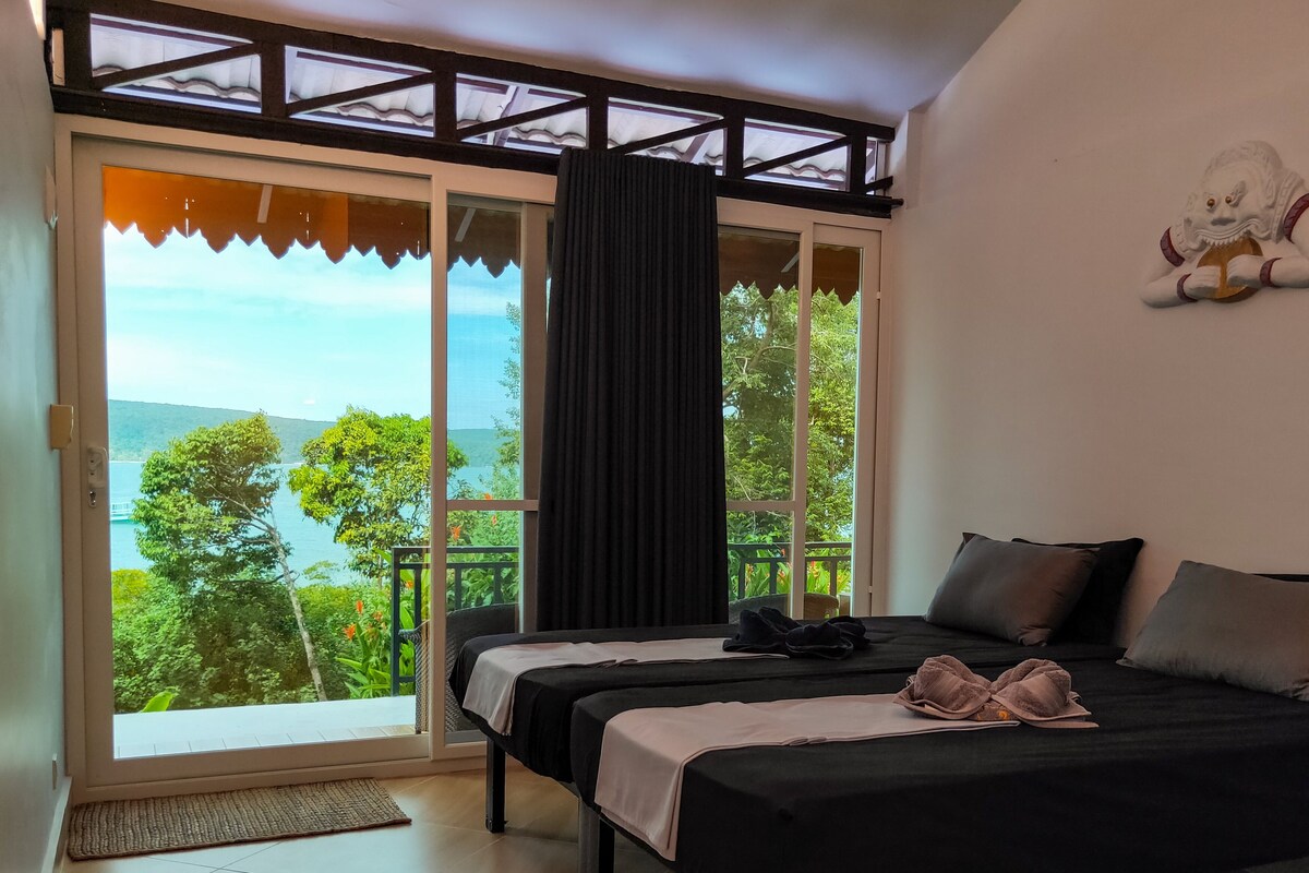 A bedroom with two beds, a view of the sea, and a decorative statue.