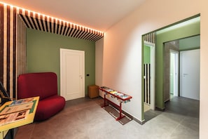 A hallway with a red upholstered chair, a small table with books, and a door with striped wallpaper. - ARCO VECCHIO URBAN SUITE by EPOCA COLLECTION (Lecce)