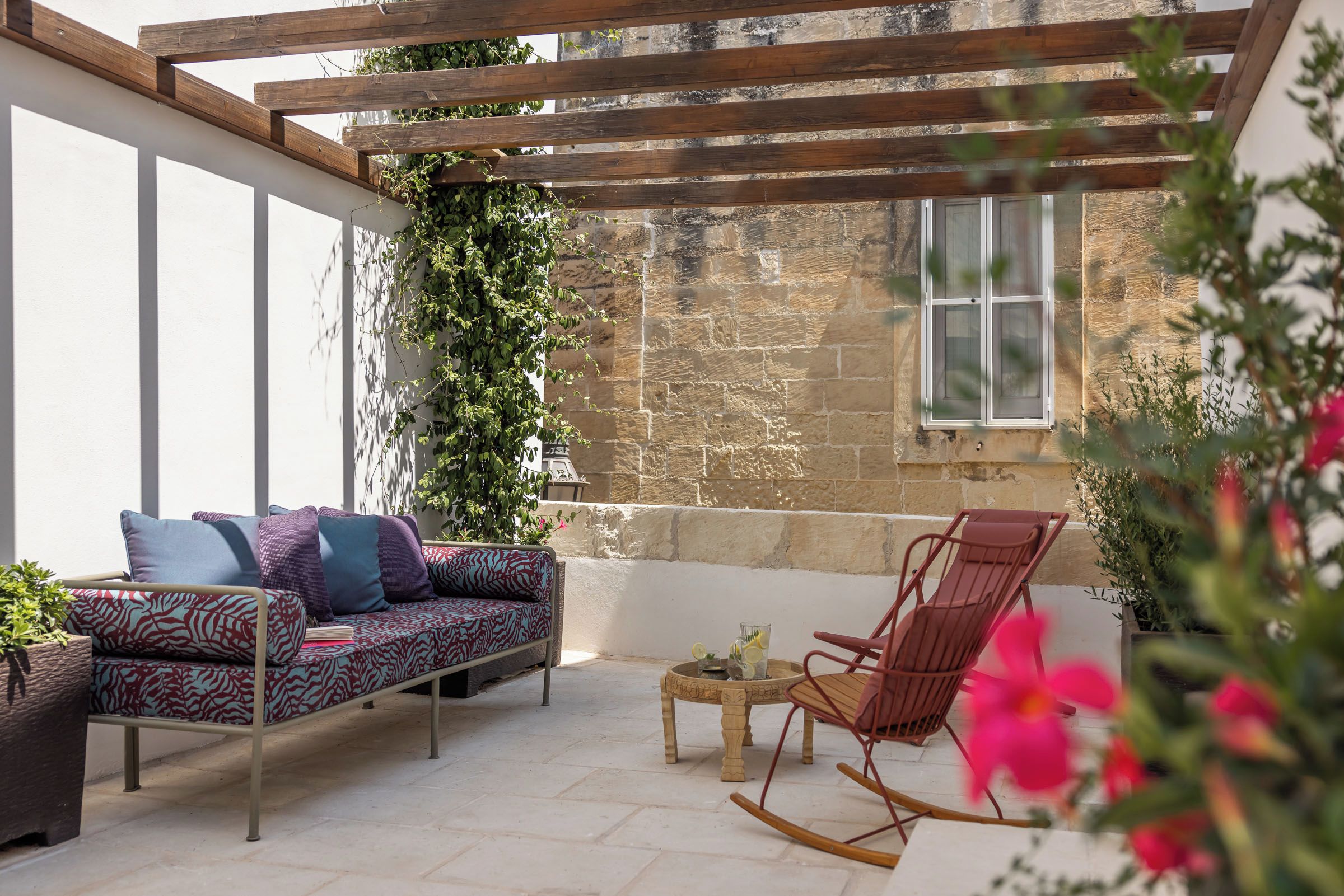 Une terrasse ensoleillée avec un canapé à motifs, un fauteuil à bascule et une petite table.
