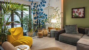 Una sala de estar moderna con un sillón amarillo, un sofá gris y diversas plantas en macetas.