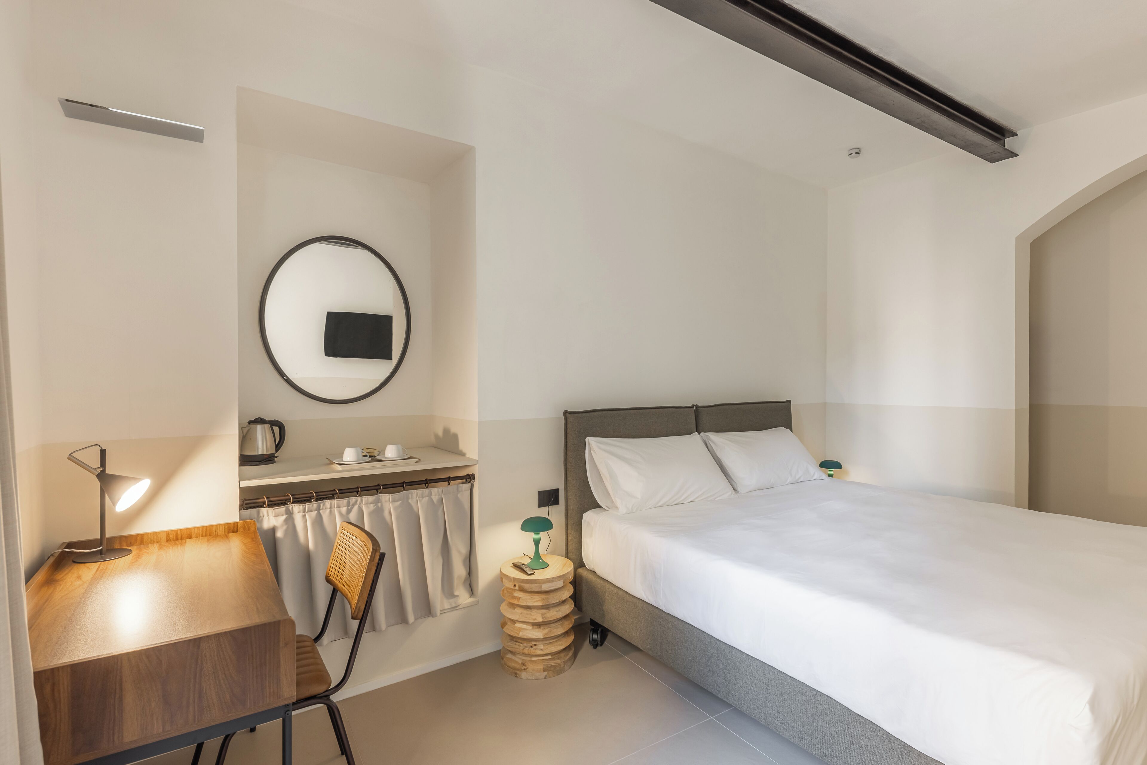 Una habitación de hotel moderna con cama, escritorio, silla y un espejo redondo en la pared.
