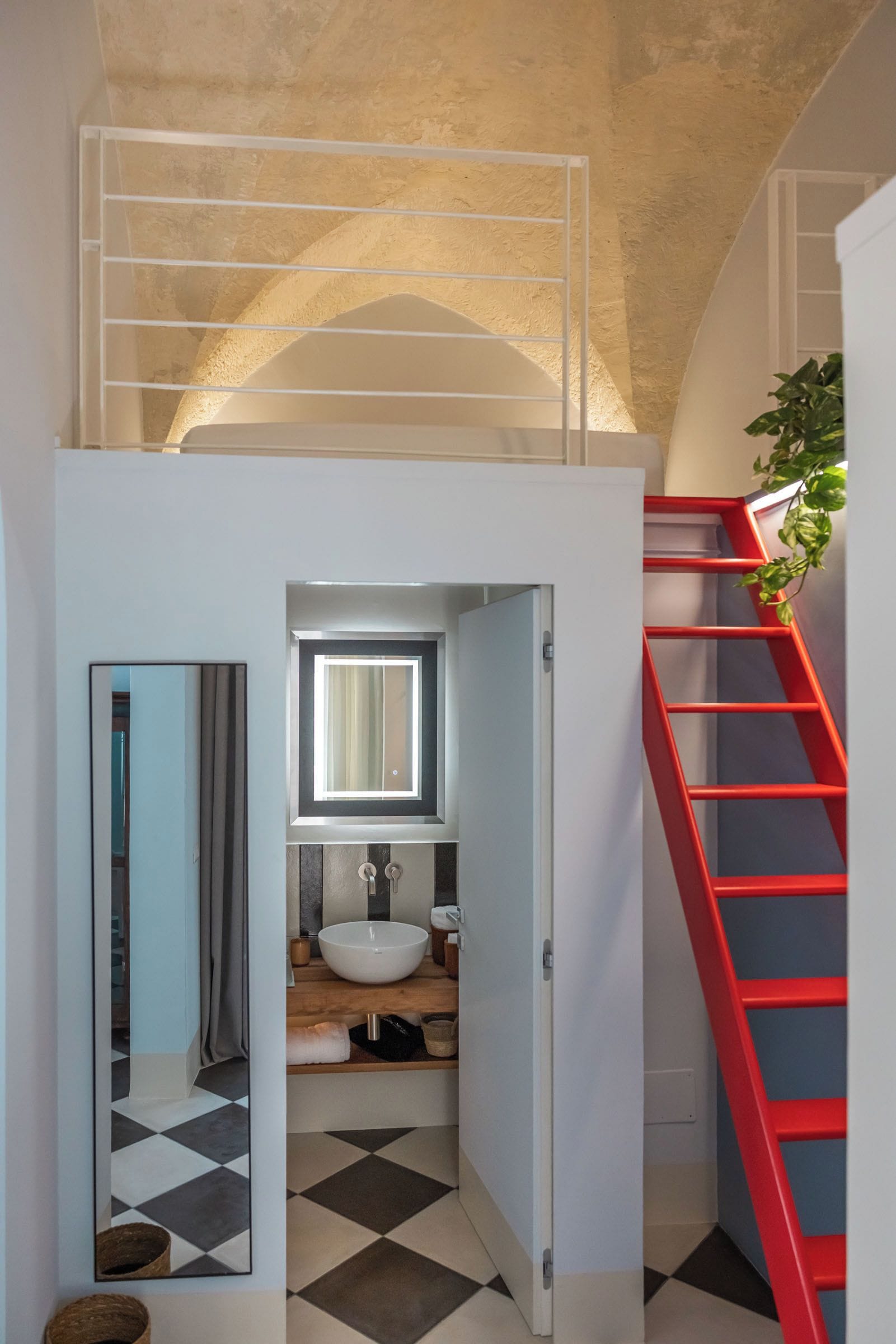 A modern bathroom with a white sink, a mirror above it, and a red staircase leading to an upper level.