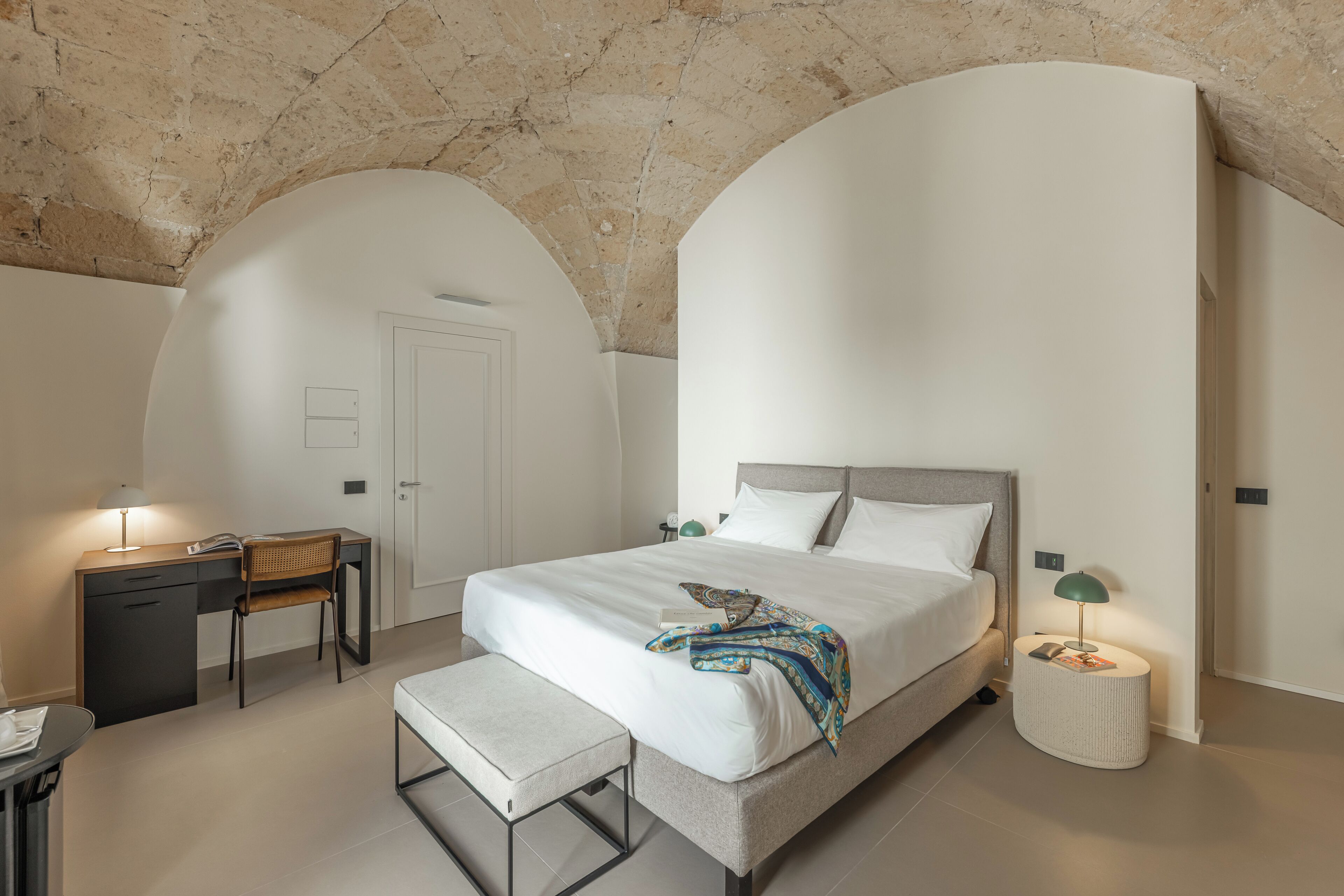 Una camera da letto moderna con un letto, un comodino, una scrivania, una sedia e una panca.