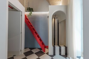 Um corredor com escada vermelha, piso em azulejo e área de chuveiro.