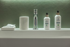 Un estante de baño con un organizador de ducha, una botella de vidrio y dos botellas de crema corporal y jabón de manos EPOCA.