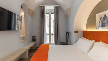 A hotel room with a large bed, a flat-screen TV mounted on the wall, a bench, and a framed picture on the wall.