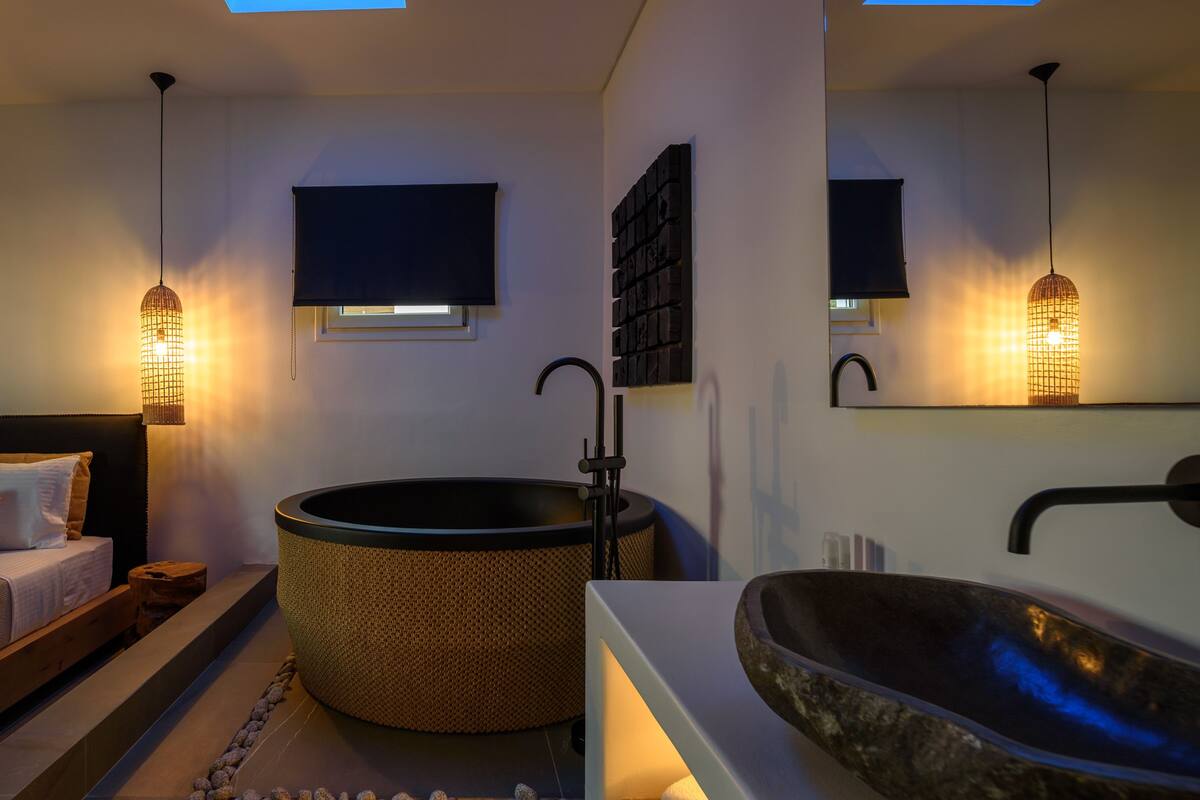 A modern bathroom with a large bathtub, a wooden bench, and a bed with pillows.