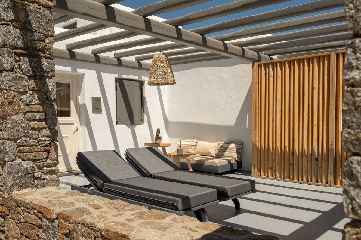 A sunlit outdoor lounge area with two reclining chairs, a small table, and a wicker lamp.