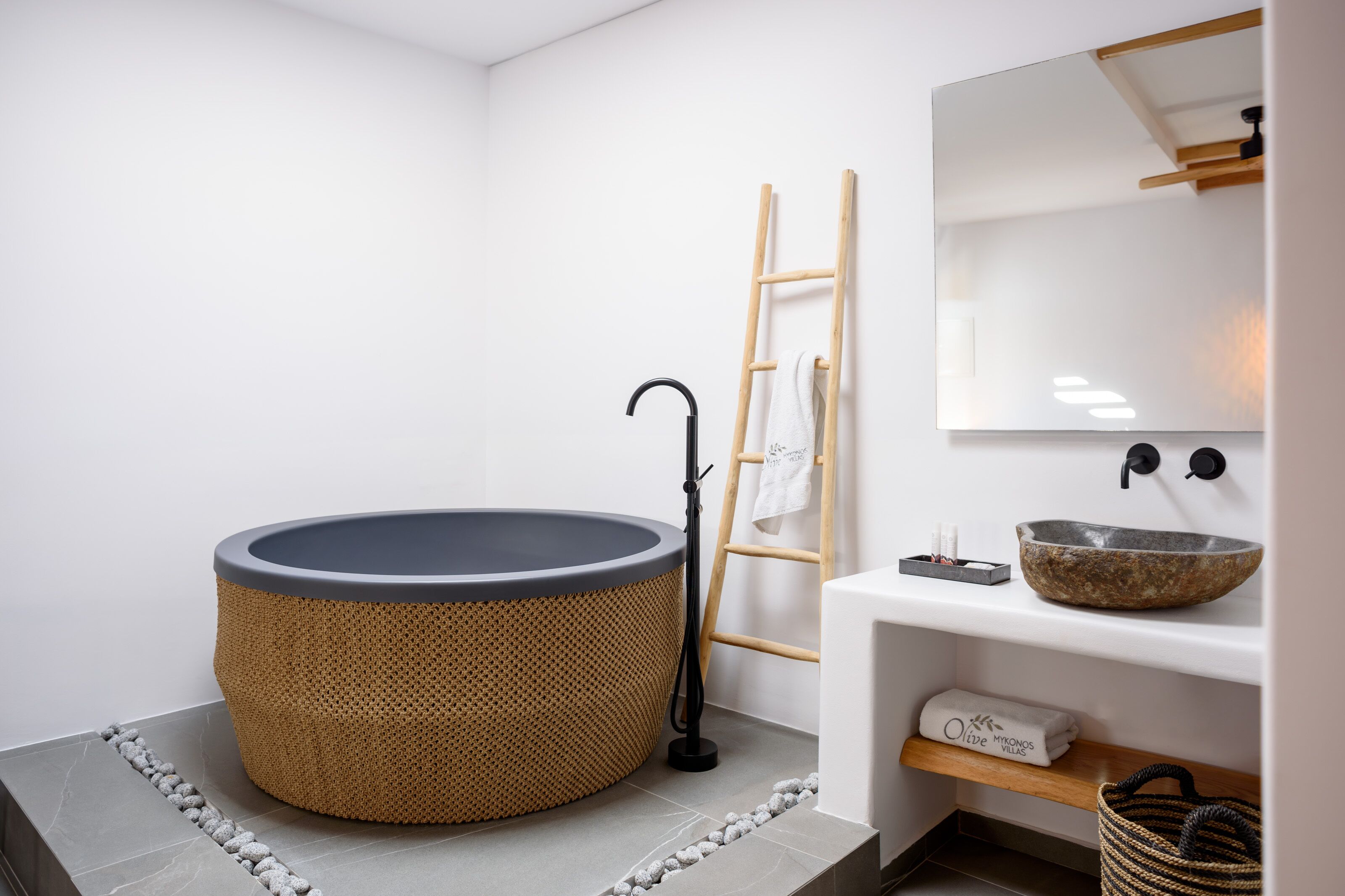 Une salle de bain moderne avec une baignoire ronde, une échelle en bois, un lavabo blanc avec un receveur en pierre et un miroir au-dessus du lavabo.