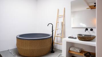Une salle de bain moderne avec une baignoire ronde, une échelle en bois, un lavabo blanc avec un receveur en pierre et un miroir au-dessus du lavabo.