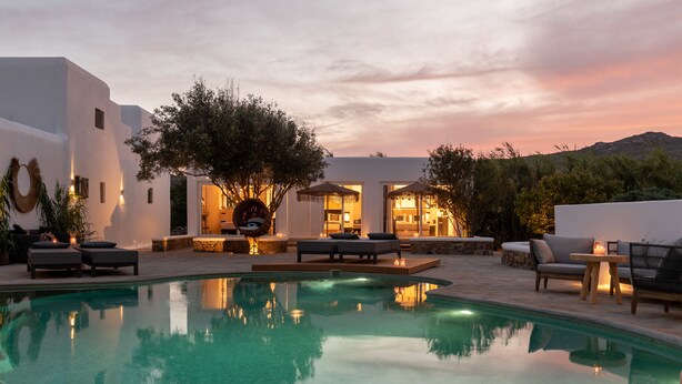 Zona junto a la piscina con mobiliario exterior y vistas al atardecer.