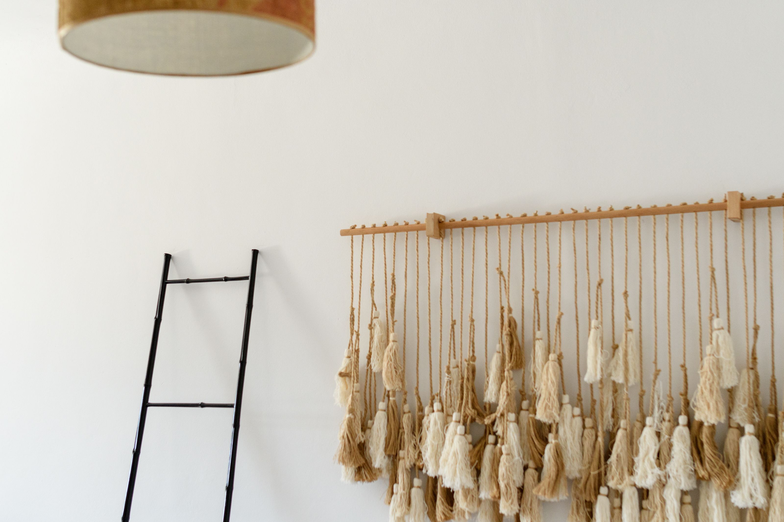 A white wall with a wooden ladder and a macramé wall hanging.
