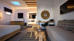 Un dormitorio moderno con cama, sofá, mesa de centro de madera, televisor y espejo.
