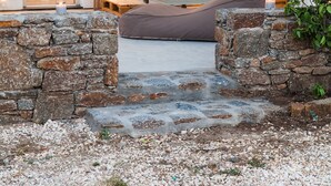 Un rincón al aire libre acogedor, con un muro de piedra, un banco de madera y una cesta de mimbre.