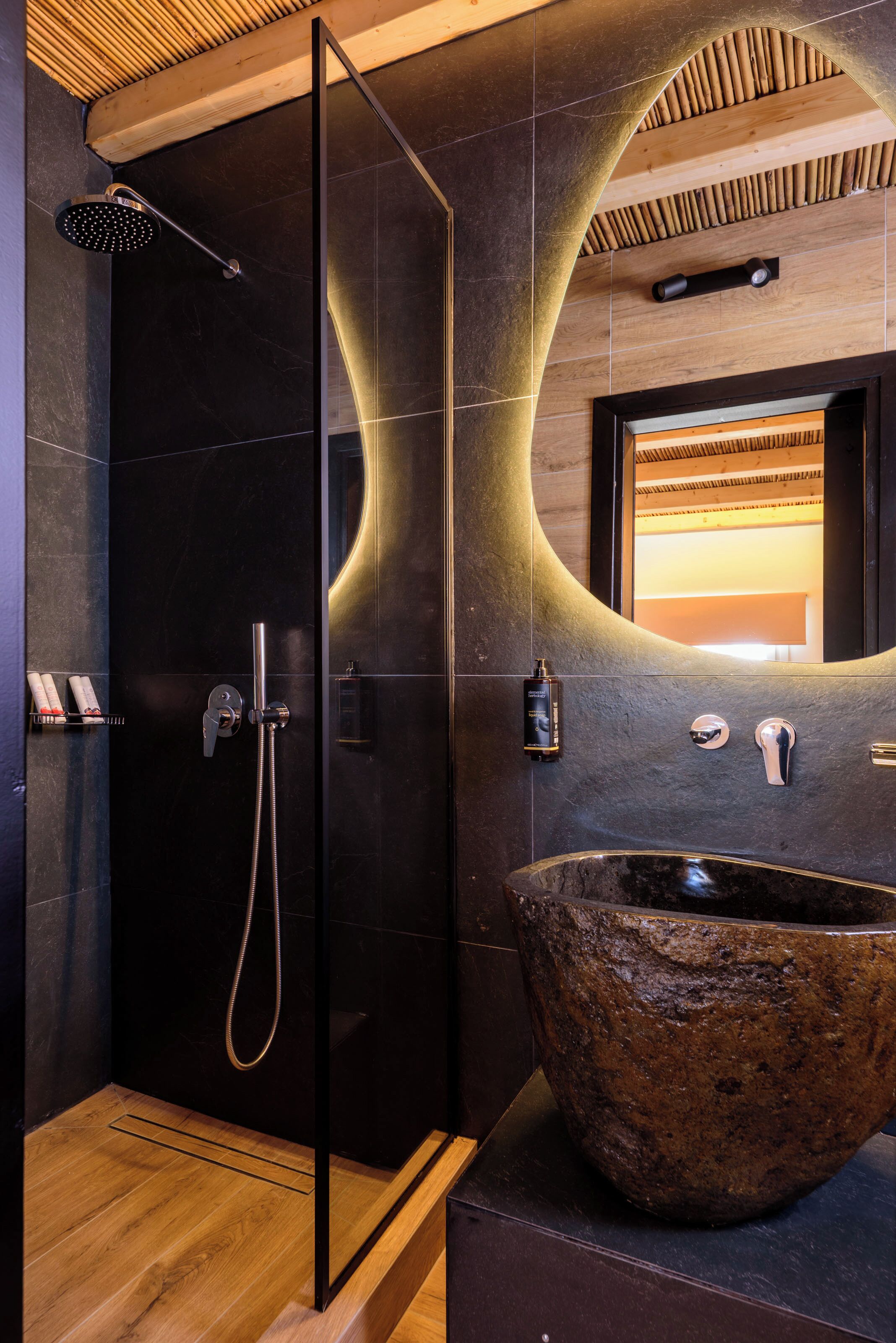 Un baño moderno con ducha envuelta en vidrio, un lavabo de piedra grande y techo de madera.