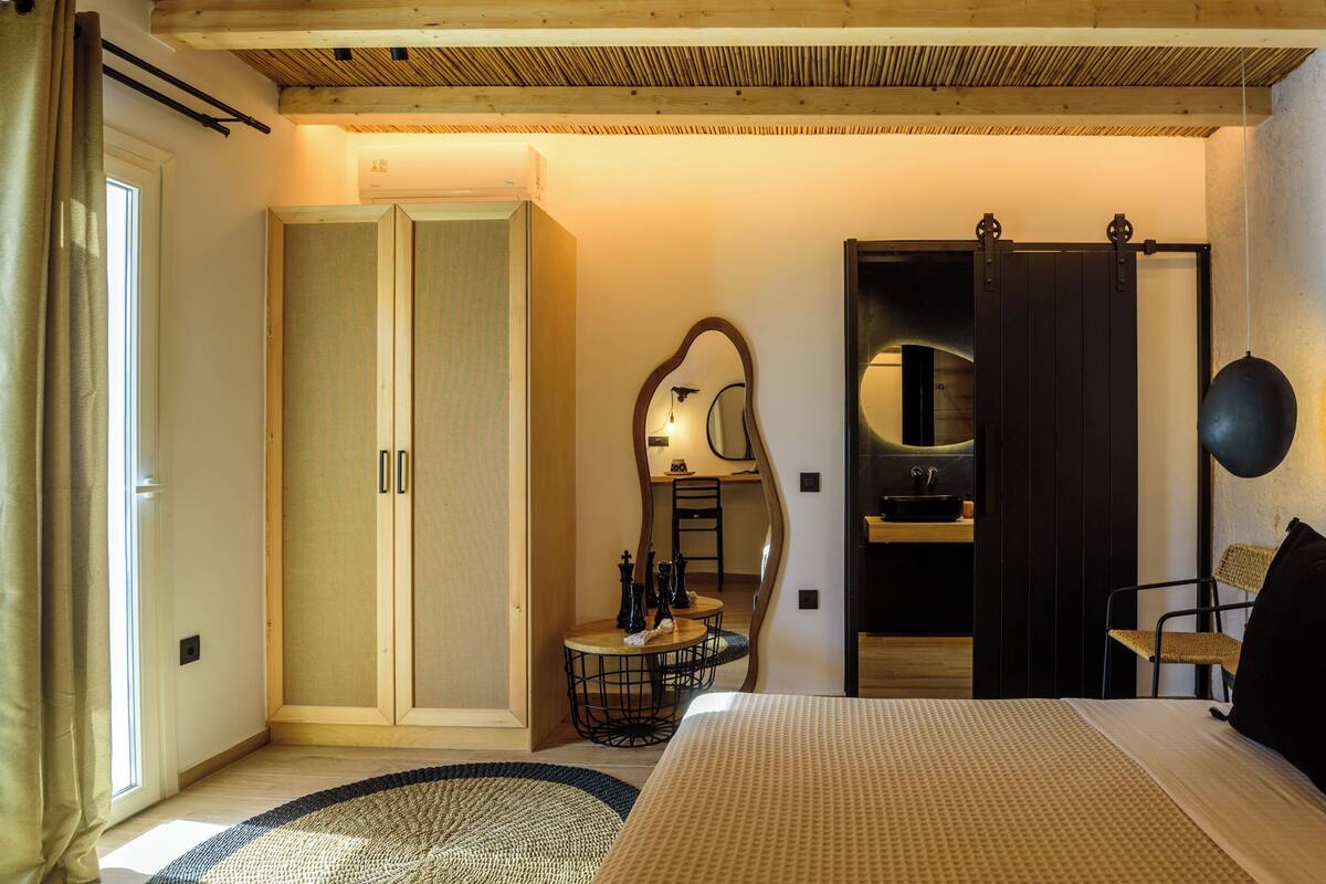A bedroom with a bed, a wardrobe, a mirror, a desk, and a window with curtains.