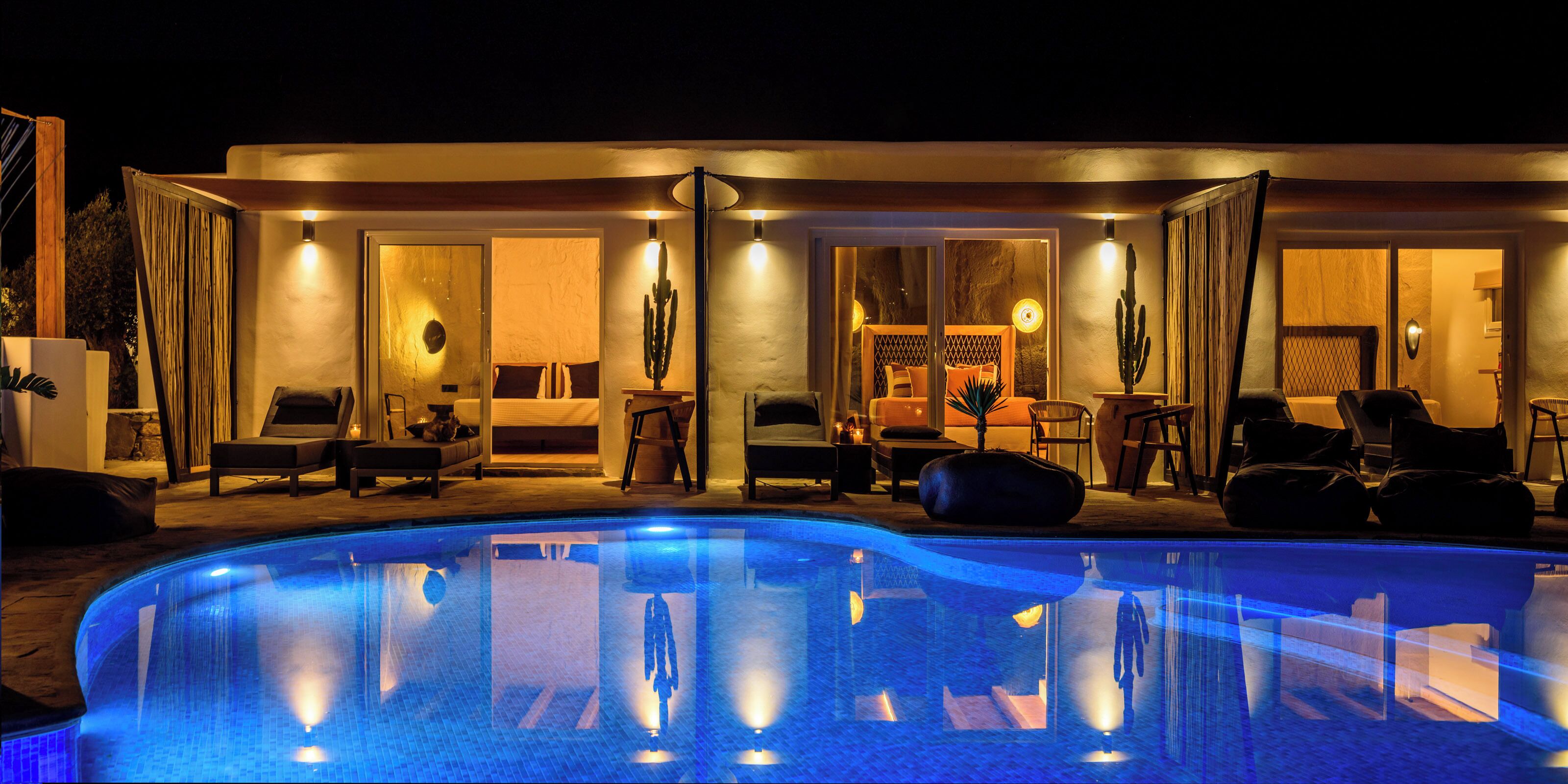 Área de piscina com espreguiçadeiras, piscina e interior bem iluminado com portas para uma sala de estar.