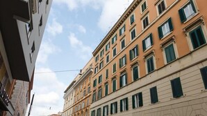 Un edificio de varios pisos con arquitectura clásica, que presenta una fila de ventanas con contraventanas verdes.