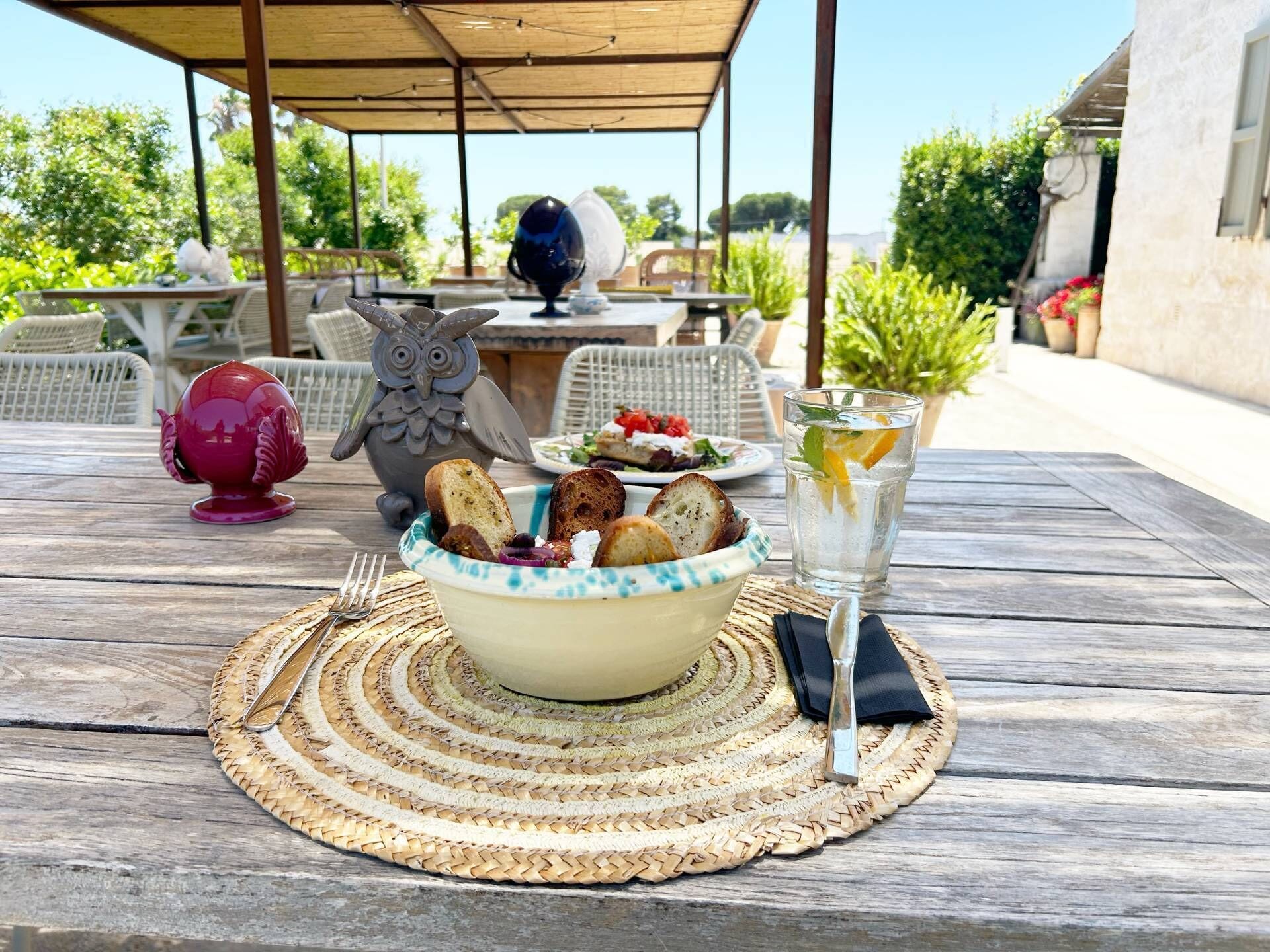 An outdoor dining area with wicker chairs, a table with a bowl of bread and salad, and a drink with a lemon slice.