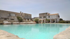 Ein Swimmingpool mit Steinrändern, umgeben von Gebäuden mit Steinmauern und Ziegeldächern.