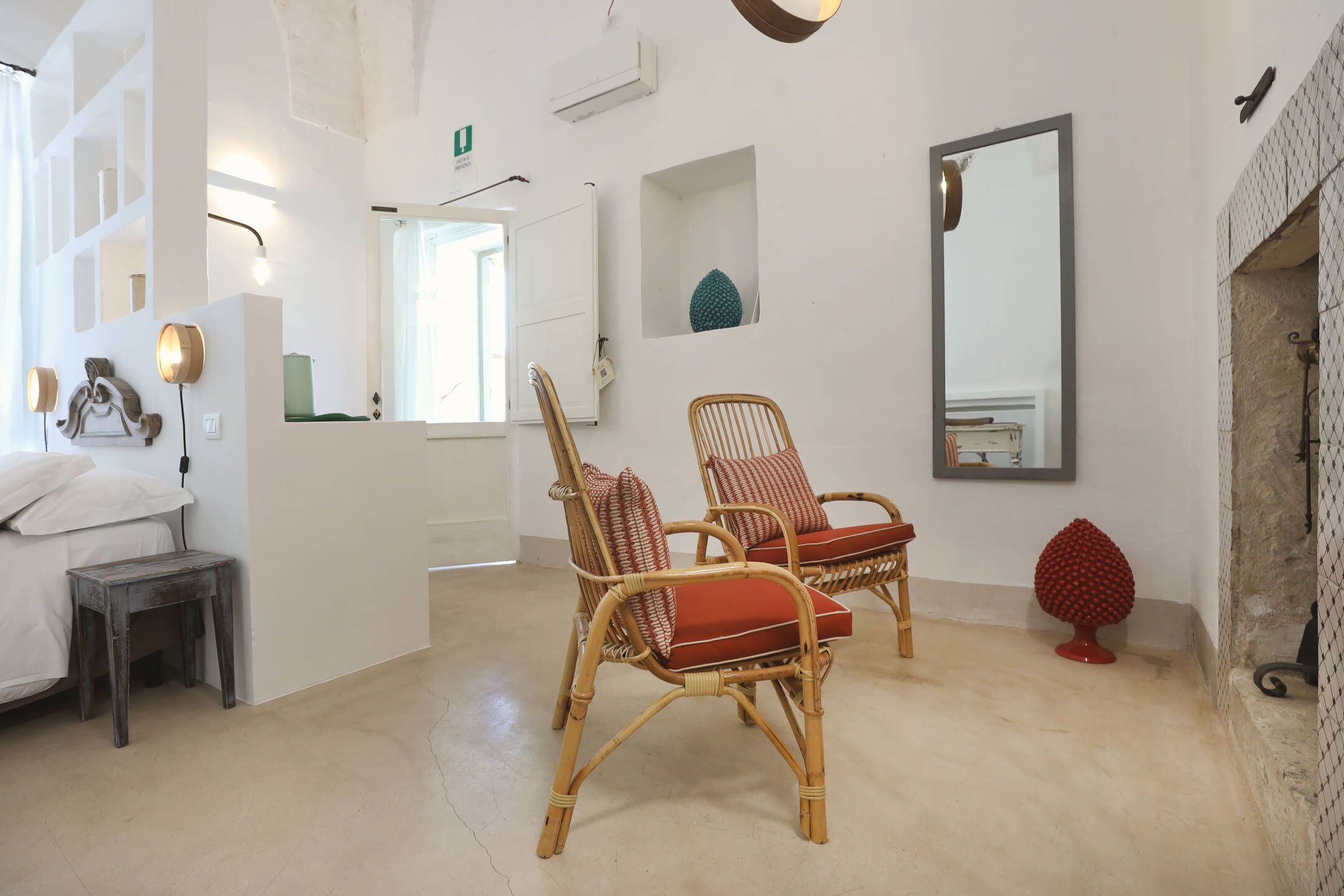 Una habitación con sillas de mimbre, una cama, una mesita, un espejo y un calentador de pared.