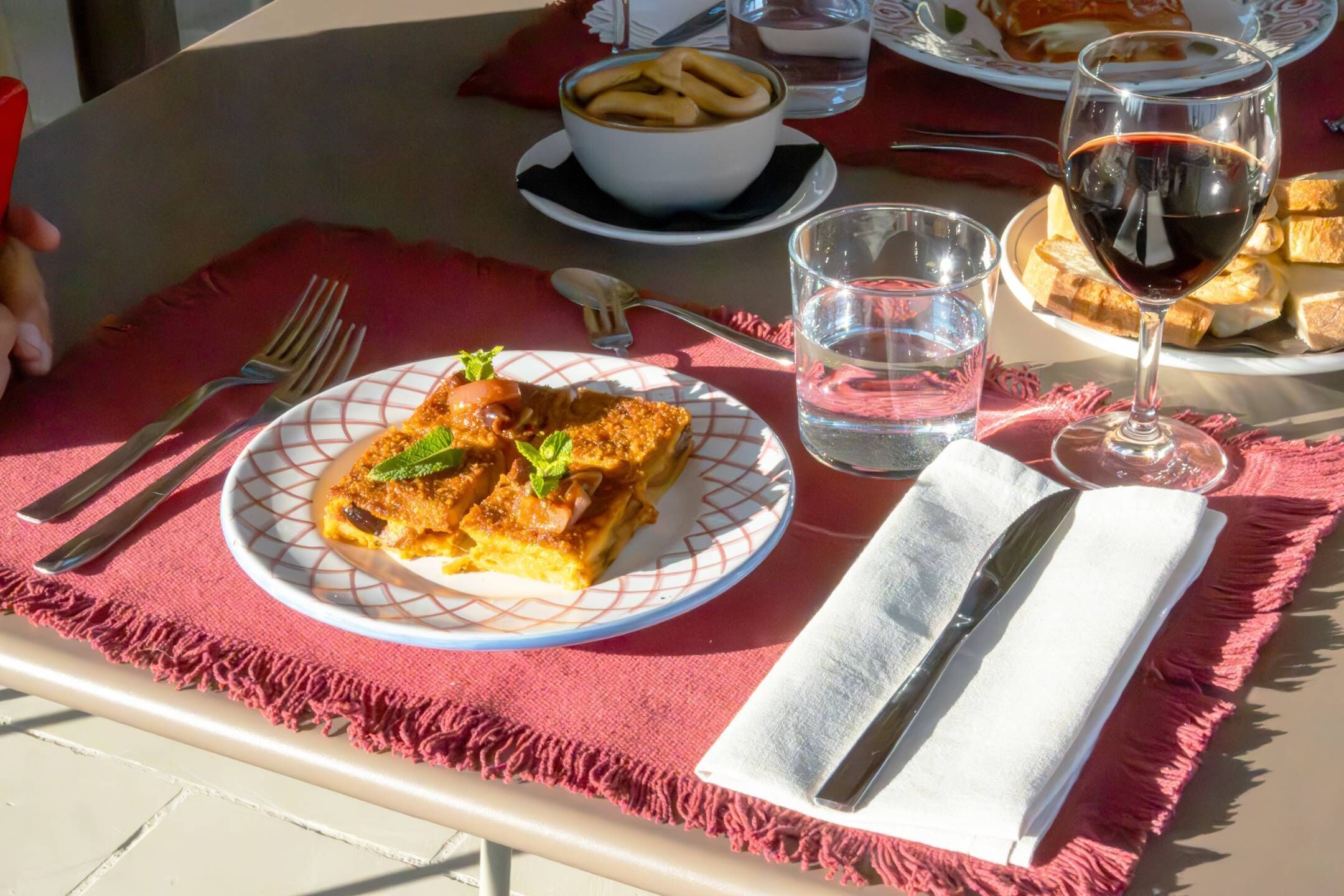 Una mesa servida con platos de comida, vasos de agua y vino, y cubiertos.