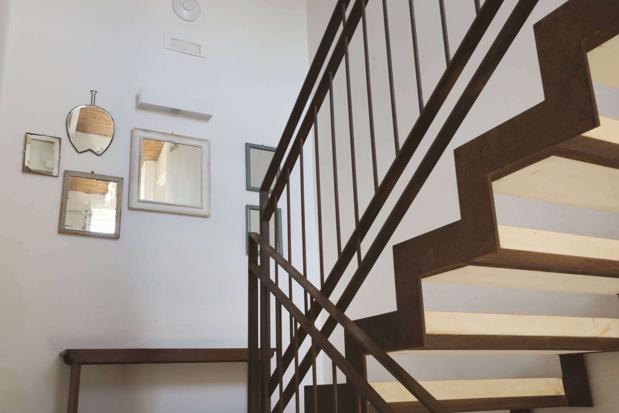 Un escalier au design géométrique, une main courante en bois et des miroirs fixés au mur.